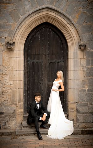 A wedding couple poses in front of a grand gothic stone archway with a traditional wooden door.