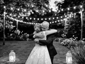 Black and white photo of newlyweds dancing under string lights at outdoor reception.