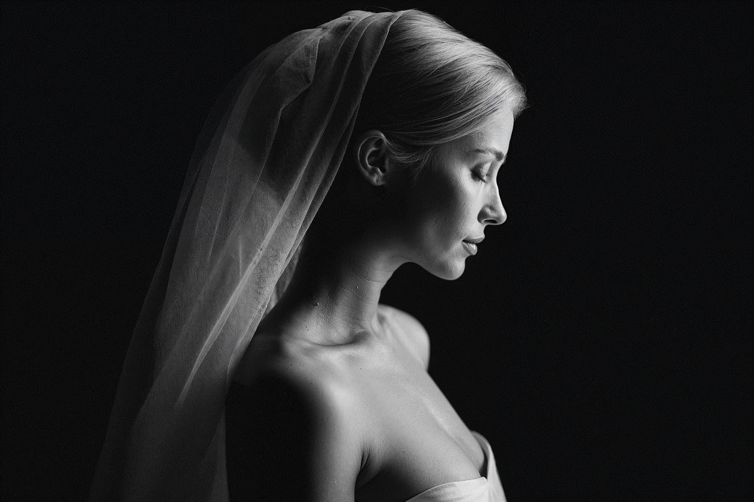 A dramatic black and white bridal portrait featuring a profile view with delicate veil details in classic lighting.