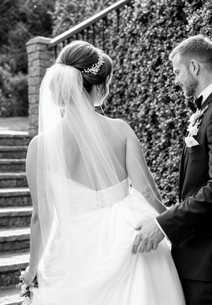 A black and white wedding photo featuring a couple on stone steps with an elegant veil and floral hairpiece.
