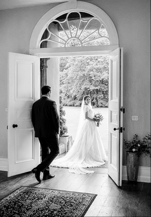 A classic black and white wedding photo framed by an elegant doorway with a fanlight window at a historic venue.