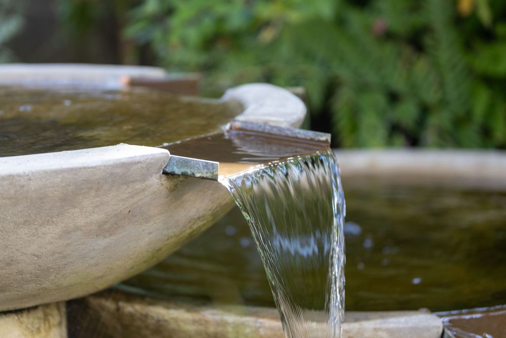 Small water spouts pour streams of clear water into a decorative garden pond feature in bright daylight.