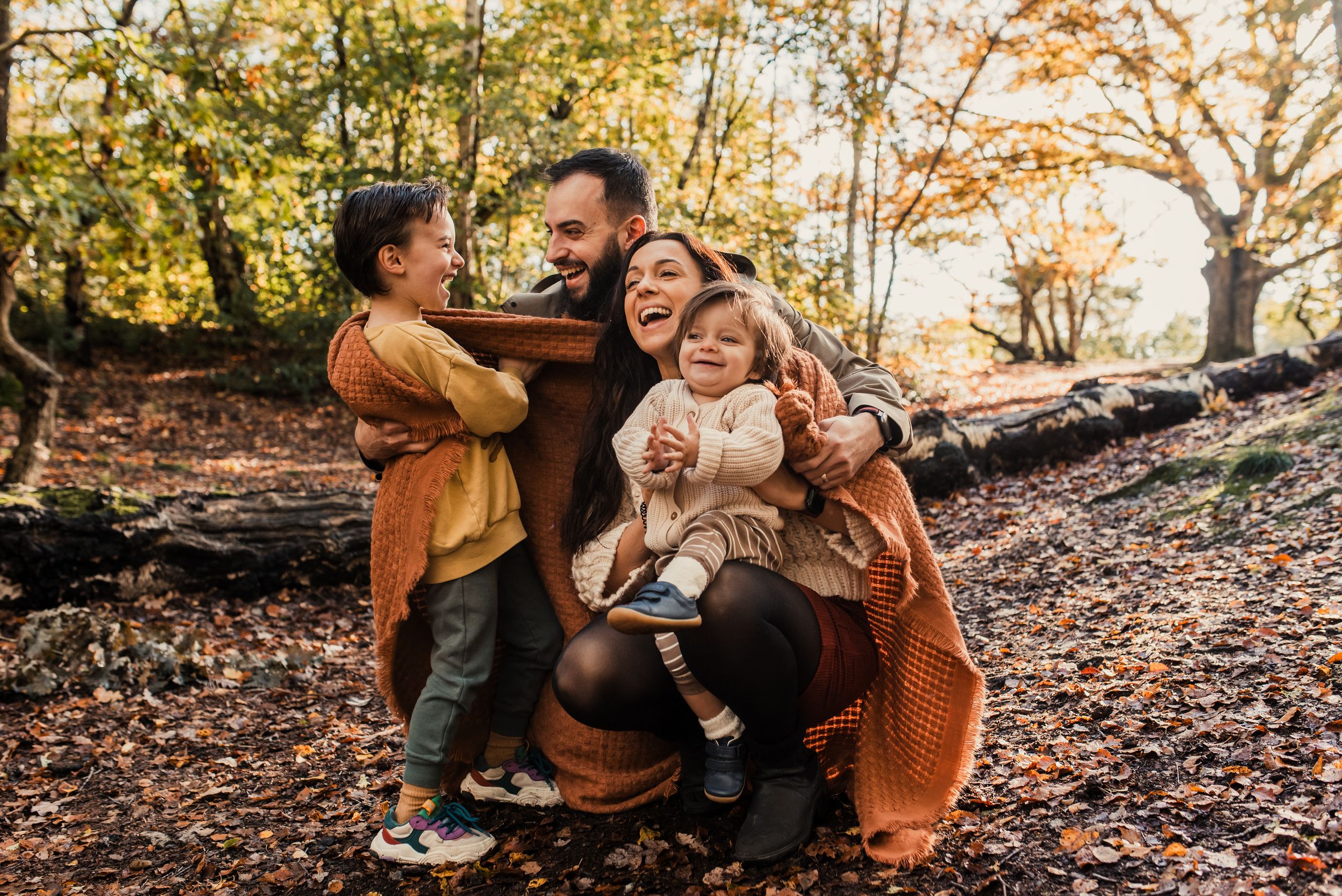 Family enjoying an autumn day together in a wooded area with fallen leaves on the ground.