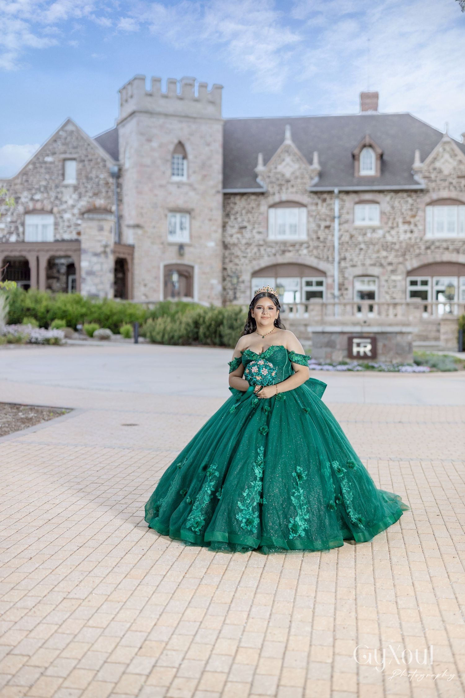 Elegant emerald green ball gown with floral details photographed in front of a stone castle-style mansion.