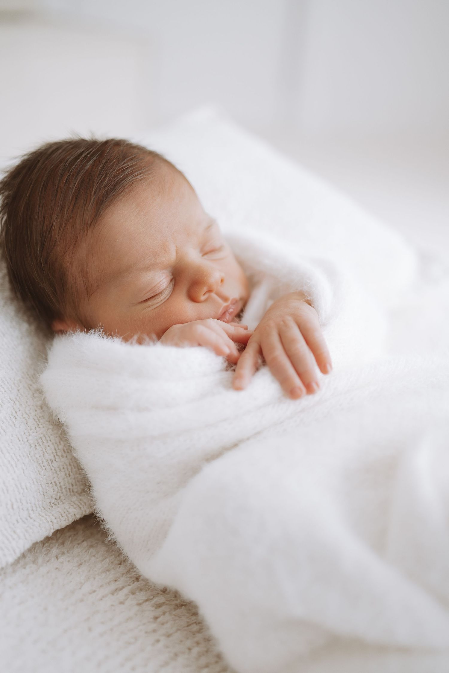 Peaceful newborn baby sleeping on white textured blanket in soft natural light.