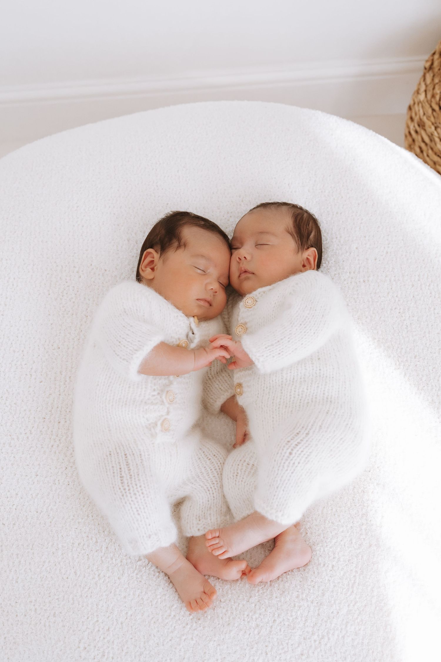 Sleeping newborn twins in white outfits lie together on soft white bedding in a series of peaceful poses.
