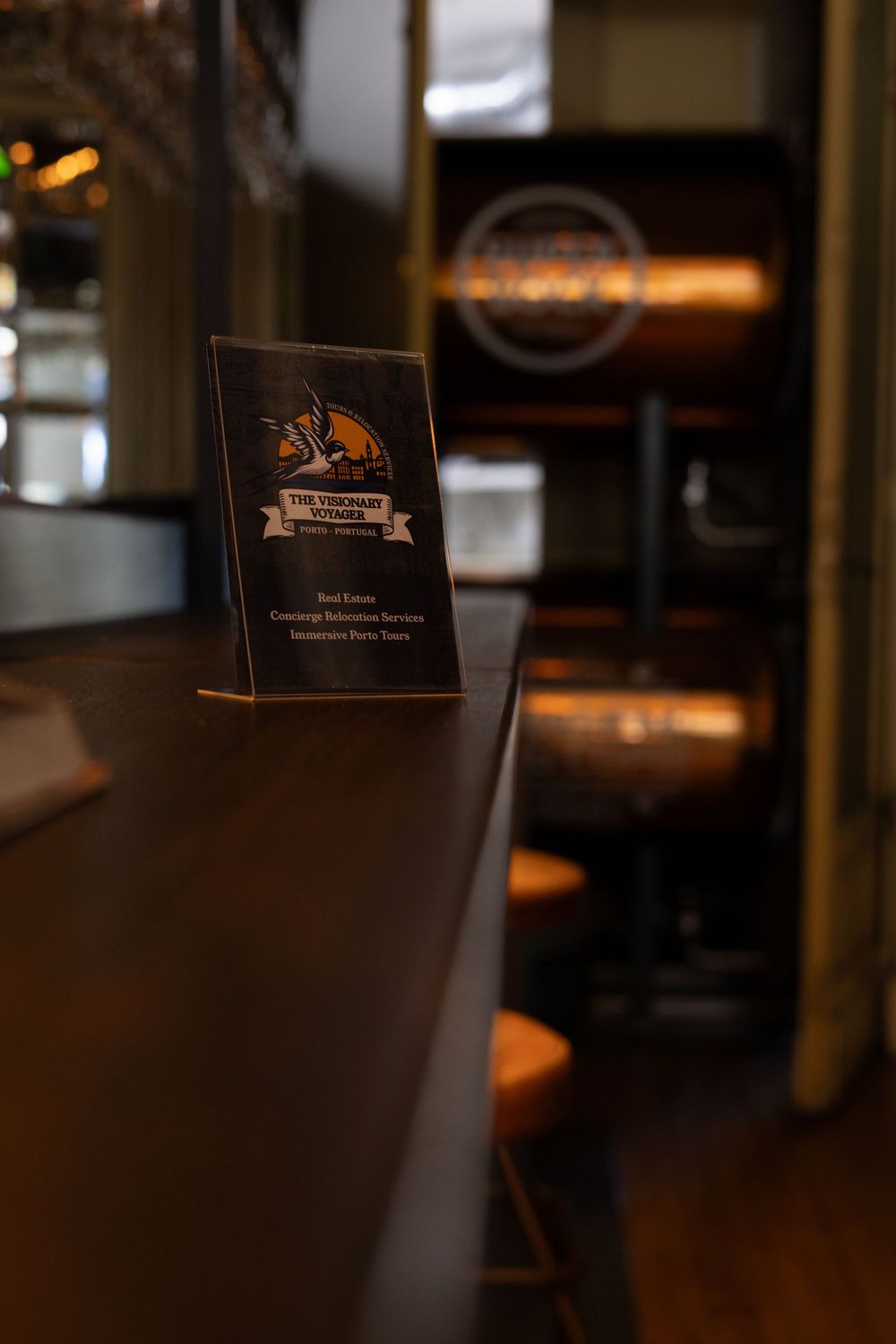 A dimly lit bar or restaurant interior with dark wood furniture and soft ambient lighting creates a cozy atmosphere.