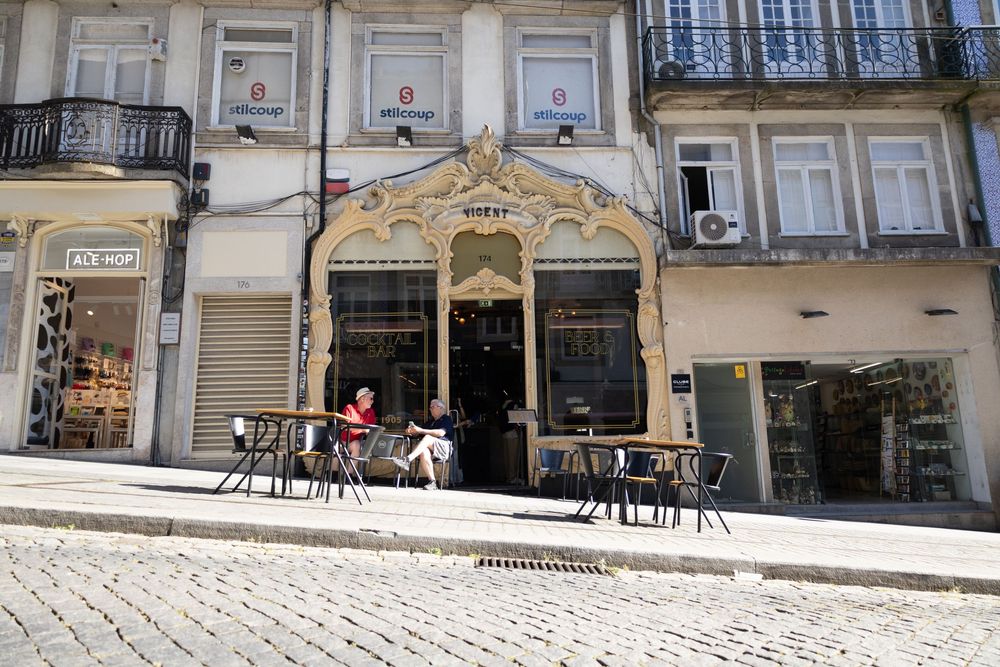 Sun-dappled cobblestone streets and classic European architecture create a charming restaurant terrace scene.