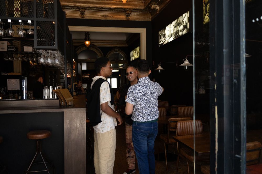 A bustling evening scene at an upscale restaurant bar with people gathering in a warmly lit interior space.