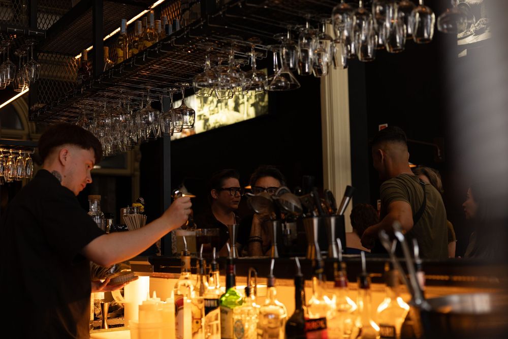 Illuminated bar counter glows warmly with candlelight and wine glasses hanging overhead in a cozy evening atmosphere.