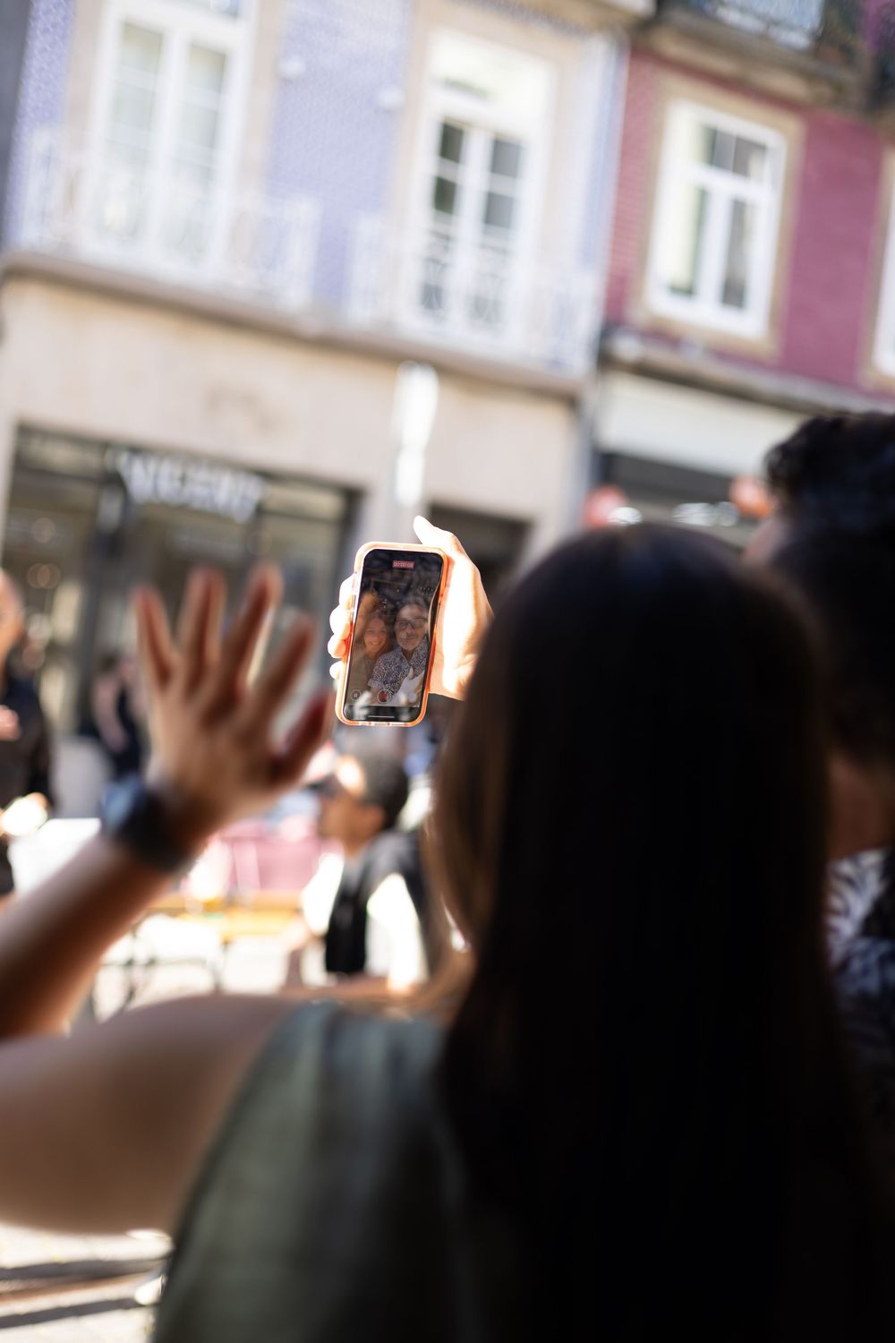 People holding up smartphones in a crowd to capture photos or video of an event in an urban setting.