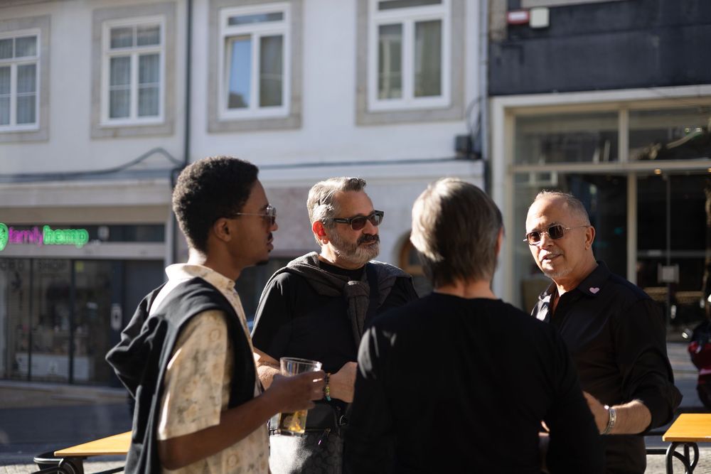 A group of friends having an animated conversation together on a sunny street outside storefronts.