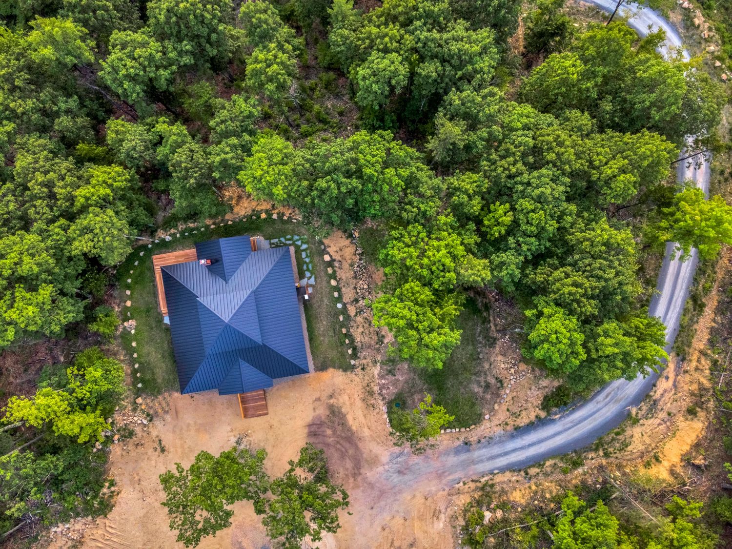 Aerial view of a blue tent structure and winding dirt road surrounded by lush green forest canopy.