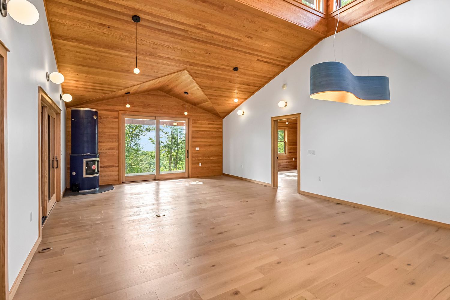 Modern open concept living room with wood ceiling, hardwood floors, and large windows offering natural light.