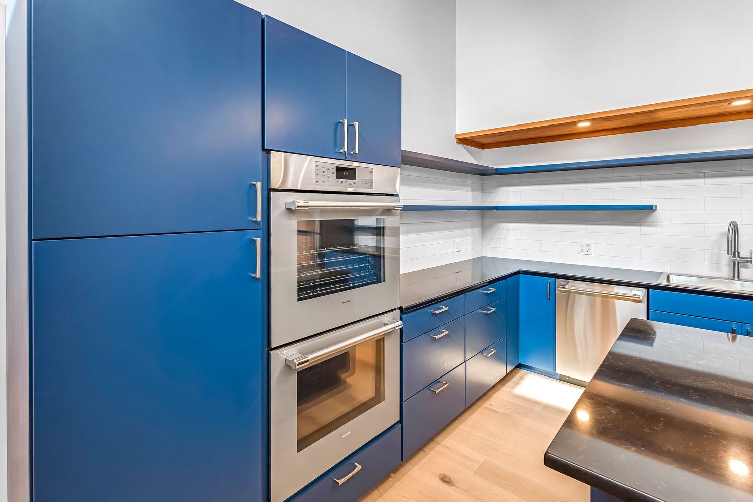 Contemporary blue kitchen featuring built-in appliances, floating shelves, and sleek cabinet design.