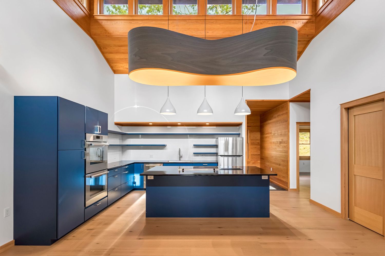 Modern kitchen with navy blue cabinets, wood accents, and a dramatic wavy pendant light over the island.
