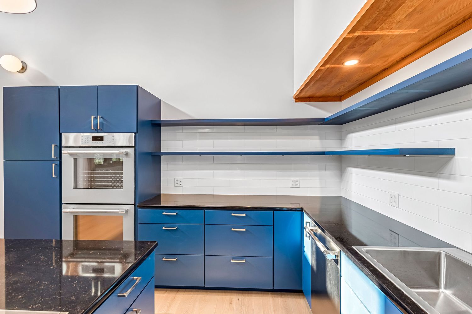 Modern kitchen with blue cabinets, black granite countertops, floating wood ceiling detail and built-in wall shelving.