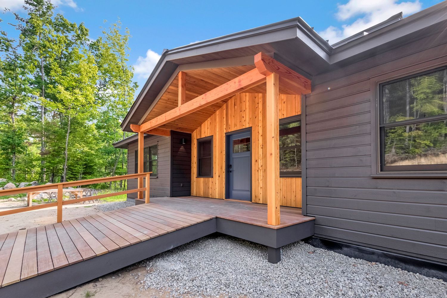 Contemporary gray house exterior with wooden porch entrance and composite deck surrounded by trees.