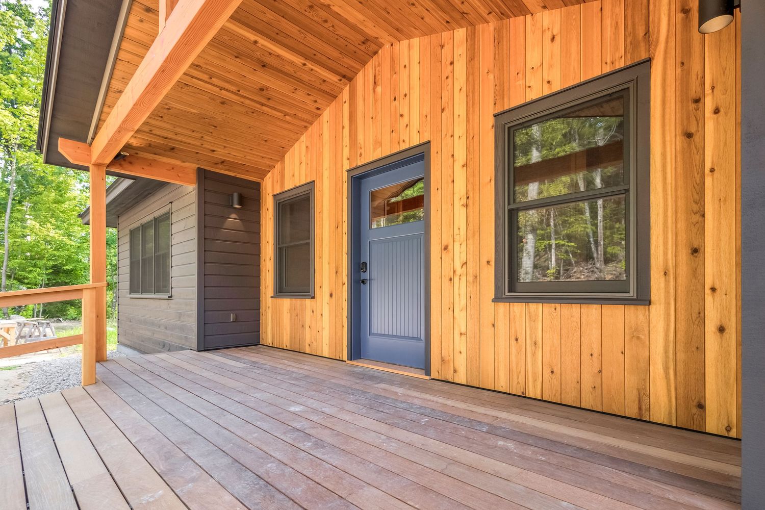 Covered wooden deck with natural cedar siding and blue door on modern home exterior.