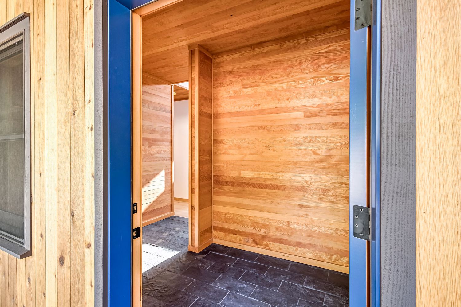 Modern entryway with blue door frame and wooden paneled walls features sleek floor tiles and warm natural lighting.