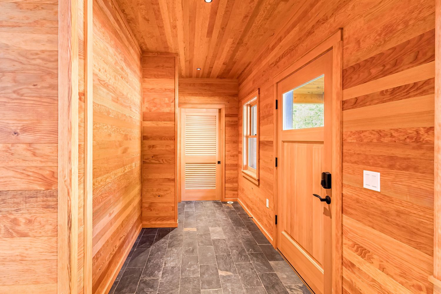 Wooden hallway with natural cedar paneling, gray floors and orange-toned doors in modern style.