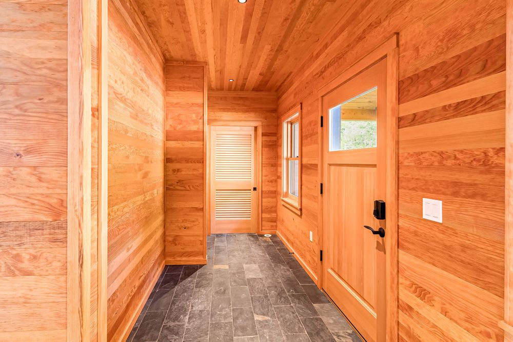 Wooden hallway with natural cedar paneling, gray floors and orange-toned doors in modern style.