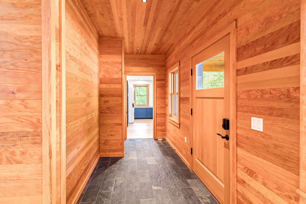 Sunlit corridor with natural wood wall paneling, slate floor tiles and a wooden door features contemporary finishes.