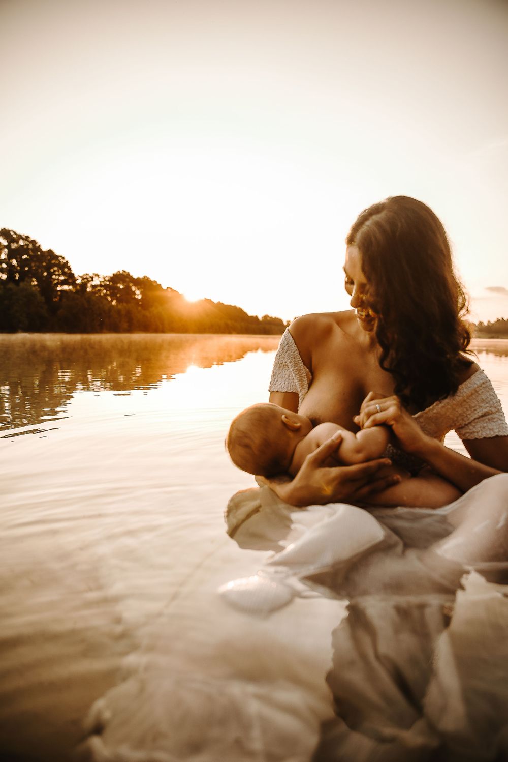A serene nursing moment captured at sunset by a lake.