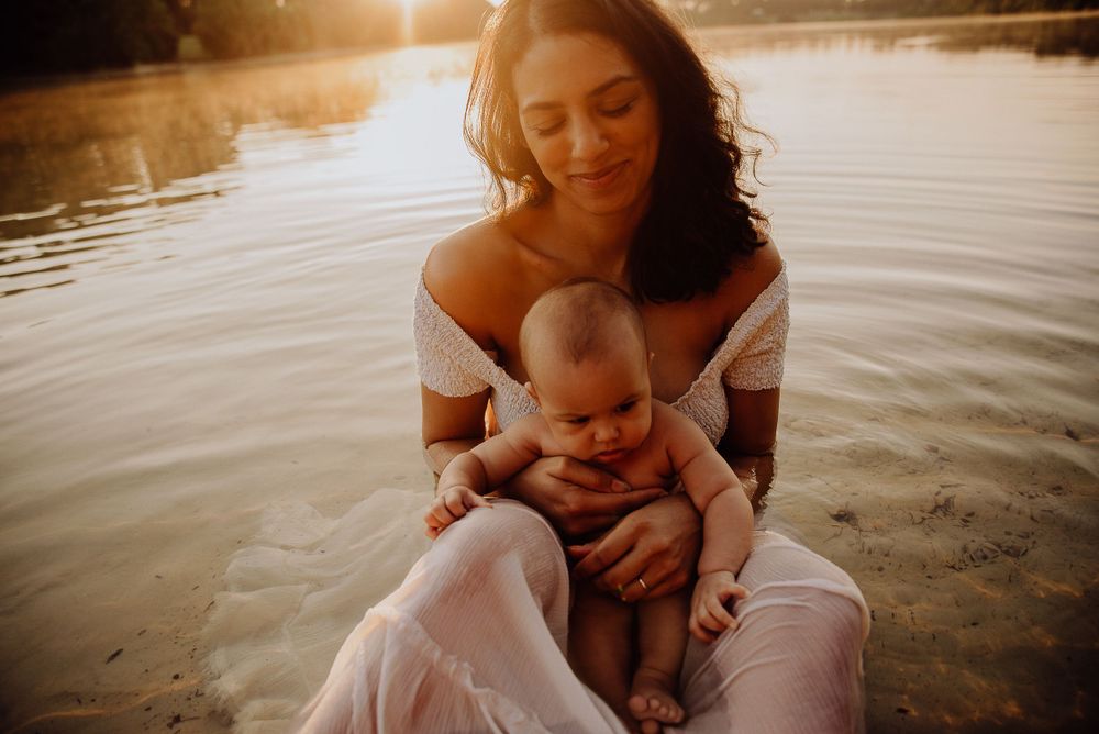 Mother and baby sitting by a tranquil lake during golden hour sunset.