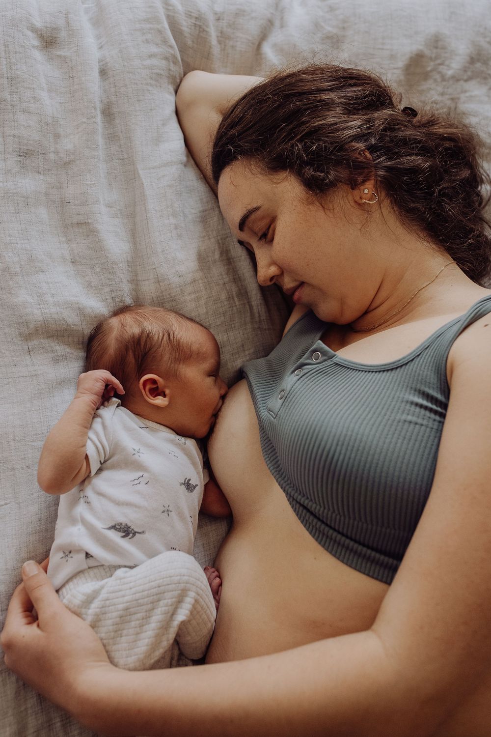 Mother and newborn baby lying together on a bed, with the infant nestled close in a peaceful bonding moment.