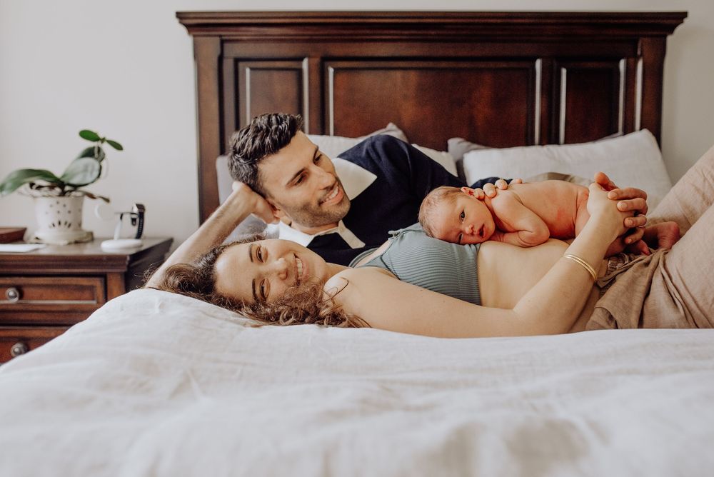 Happy parents lying on bed with their newborn baby, sharing a tender family moment in a cozy bedroom.