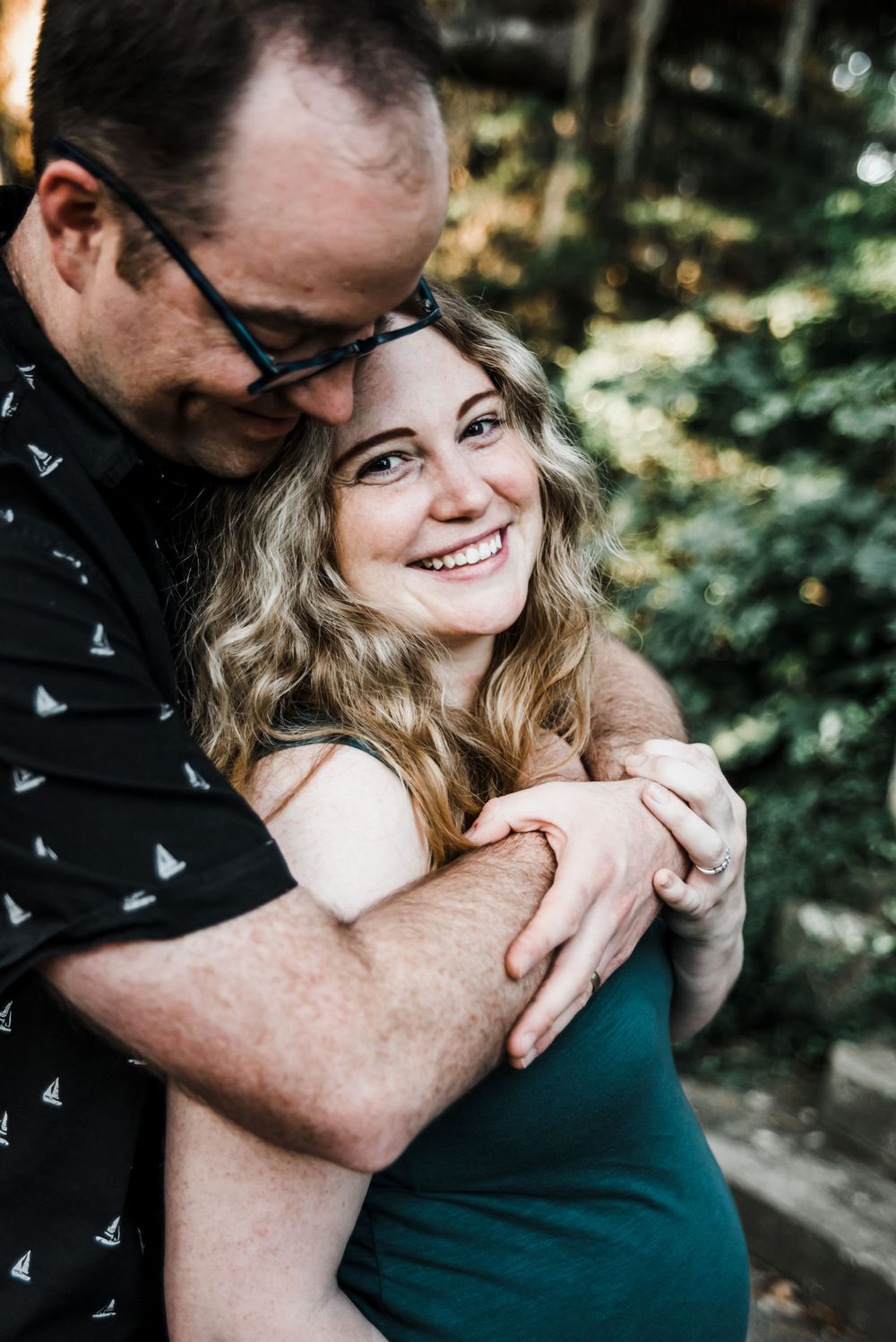Couple sharing embrace outdoors with sunlight filtering through trees.