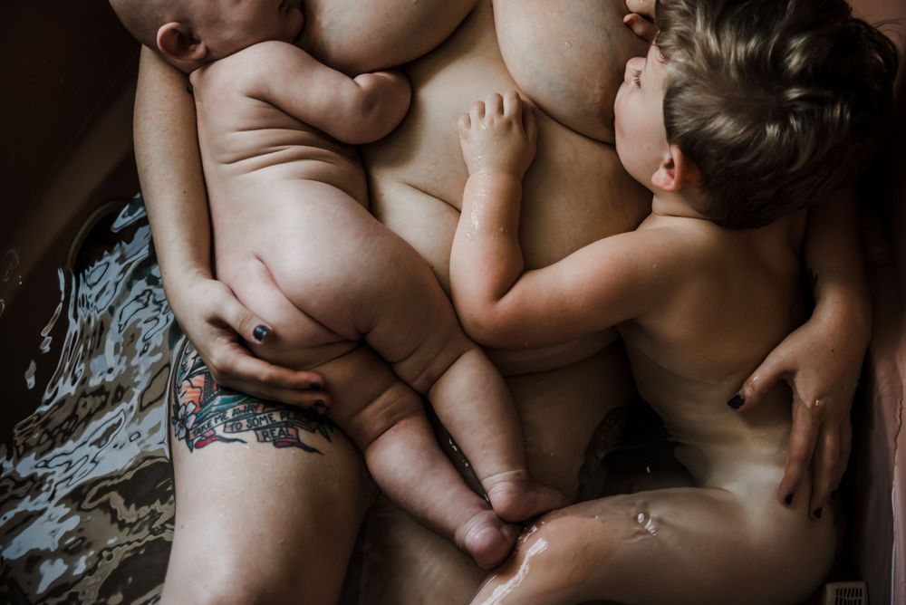 Two infants snuggle close together on soft bedding in an intimate moment.