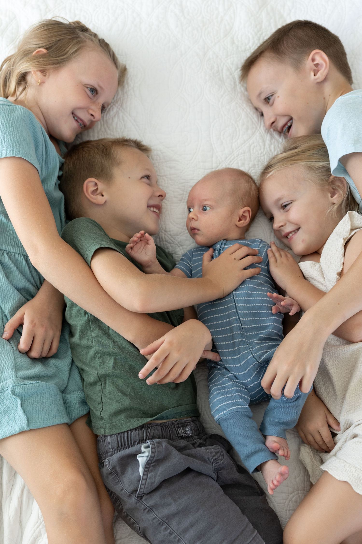 5 siblings varying age lying on a bed smiling at each other