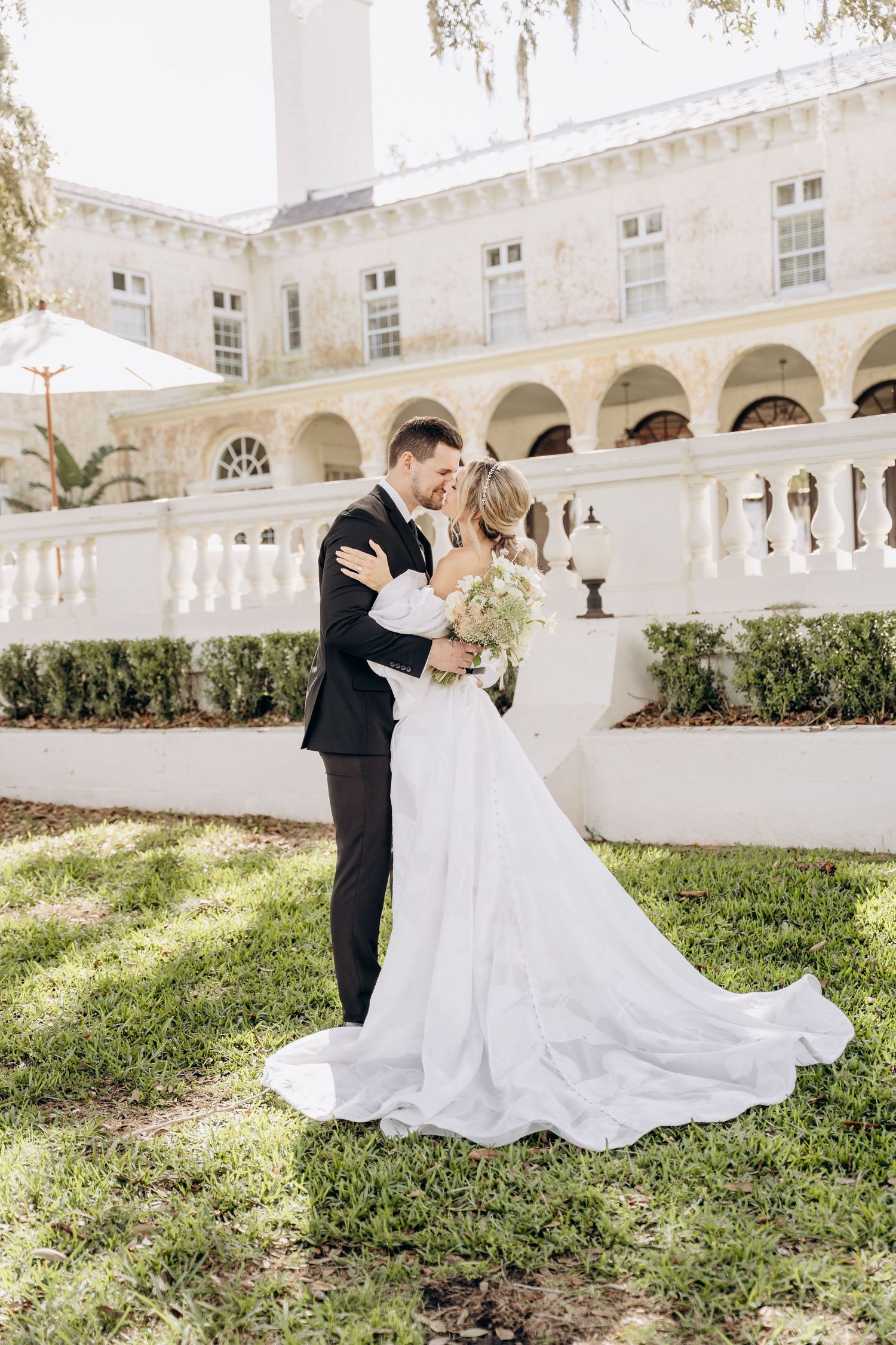 Romantic wedding couple embracing on the grounds of a grand stone building with arched architecture.