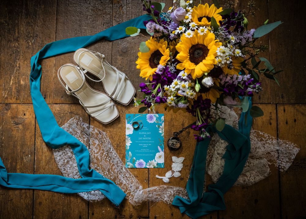 Wedding details flatlay with sunflowers, blue ribbons and accessories on wooden surface.