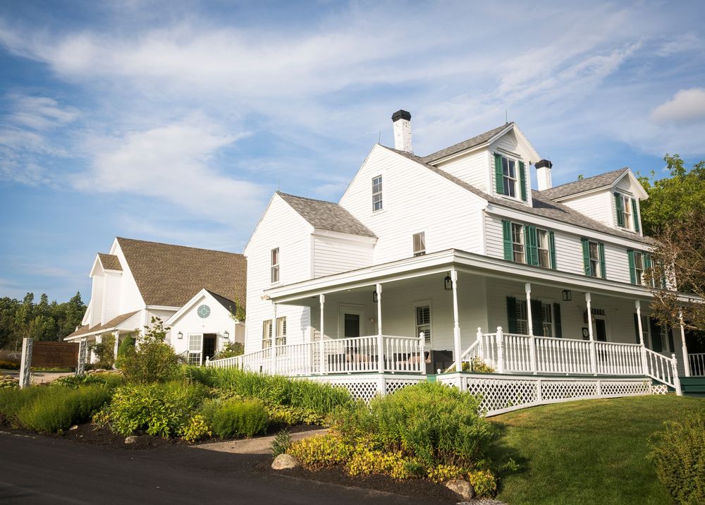 A series of five white residential houses with covered porches set against a blue sky and green landscaping.