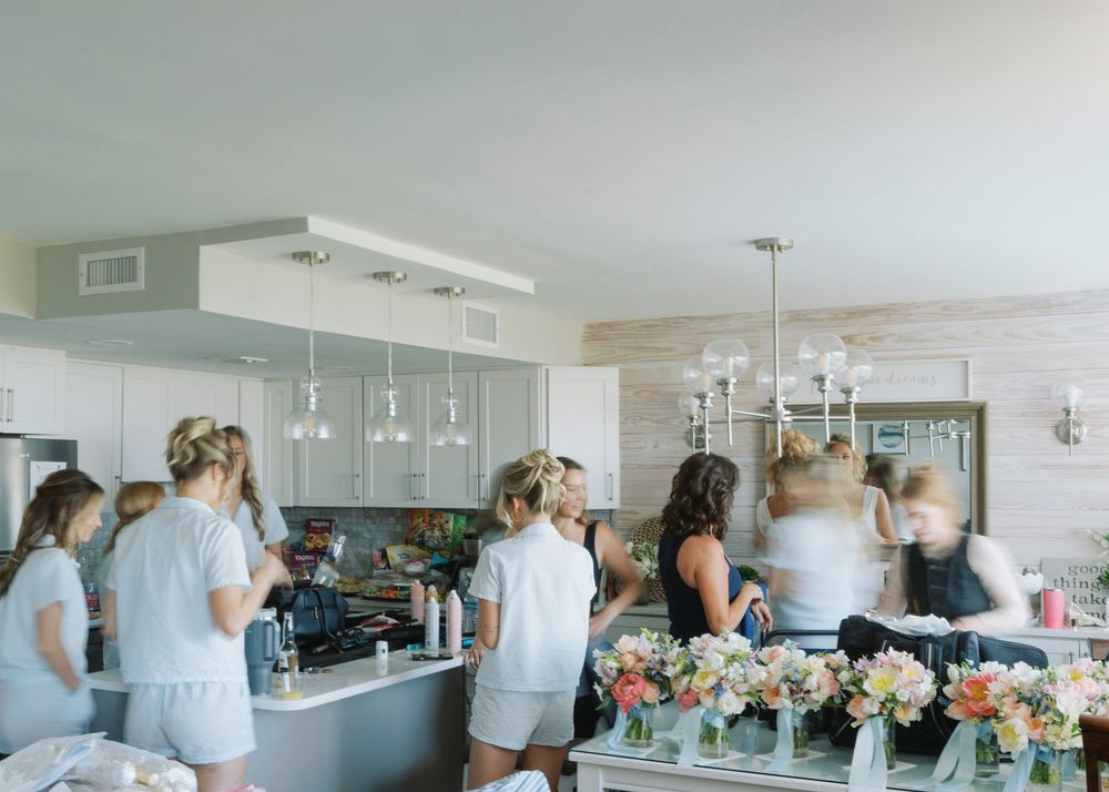 Bridesmaids in white getting ready together in bright modern suite with floral arrangements.