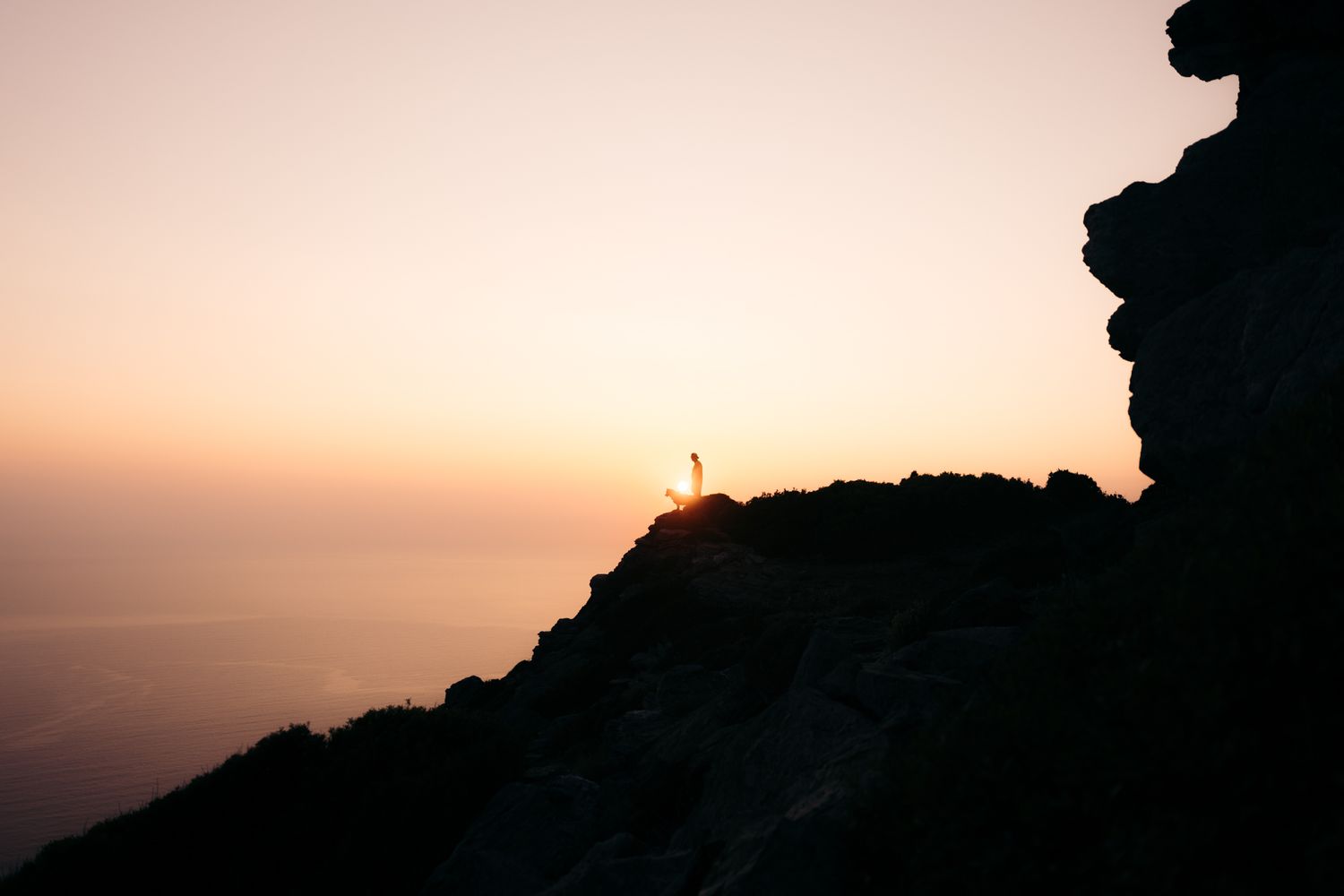 coucher de soleil au moulin mattei, on voit une silhouette d'un homme et son chien en haut des falaises avec les lumières orangées
