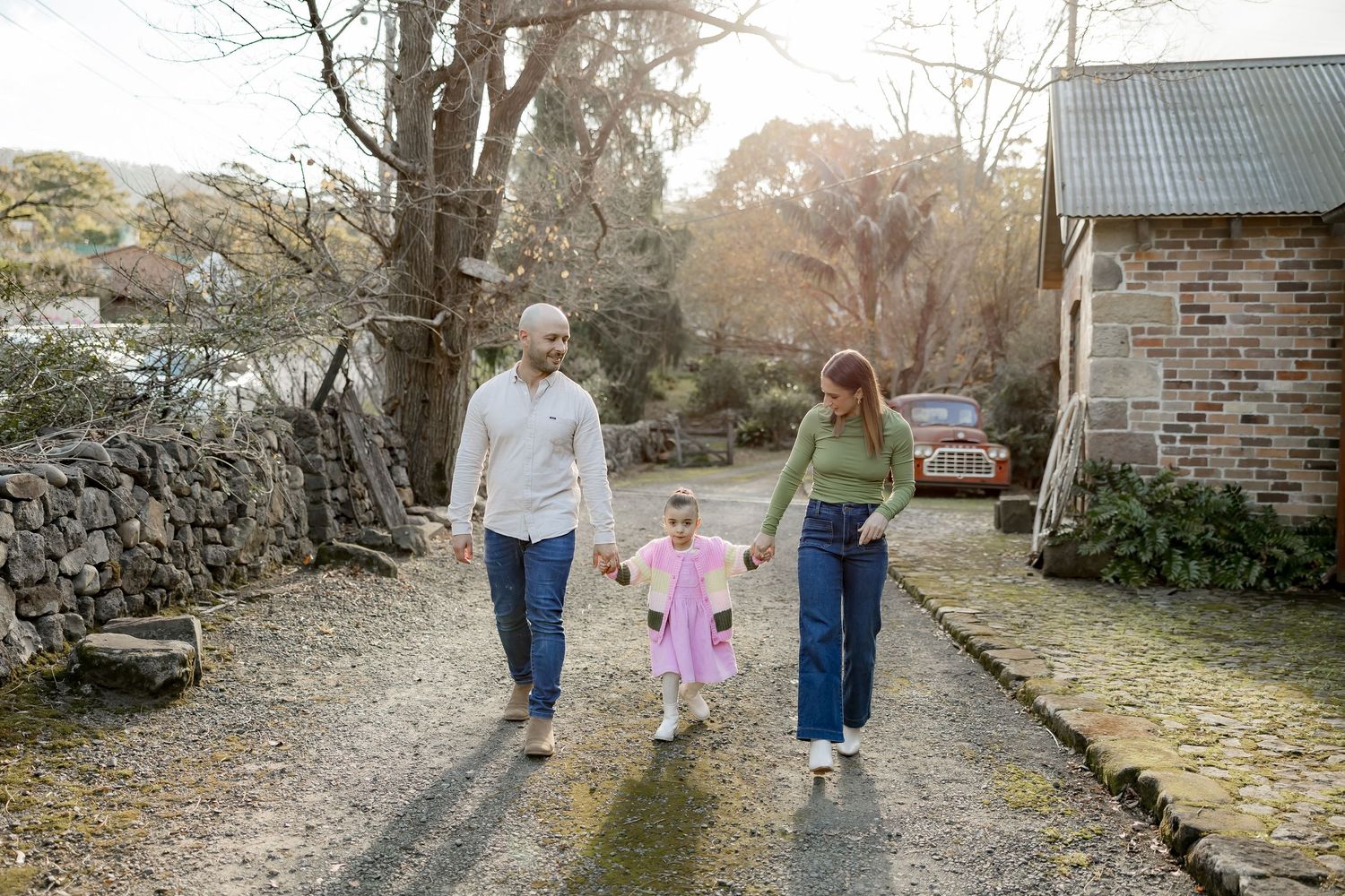 A family holds hands while walking together along a scenic stone wall path at sunset.