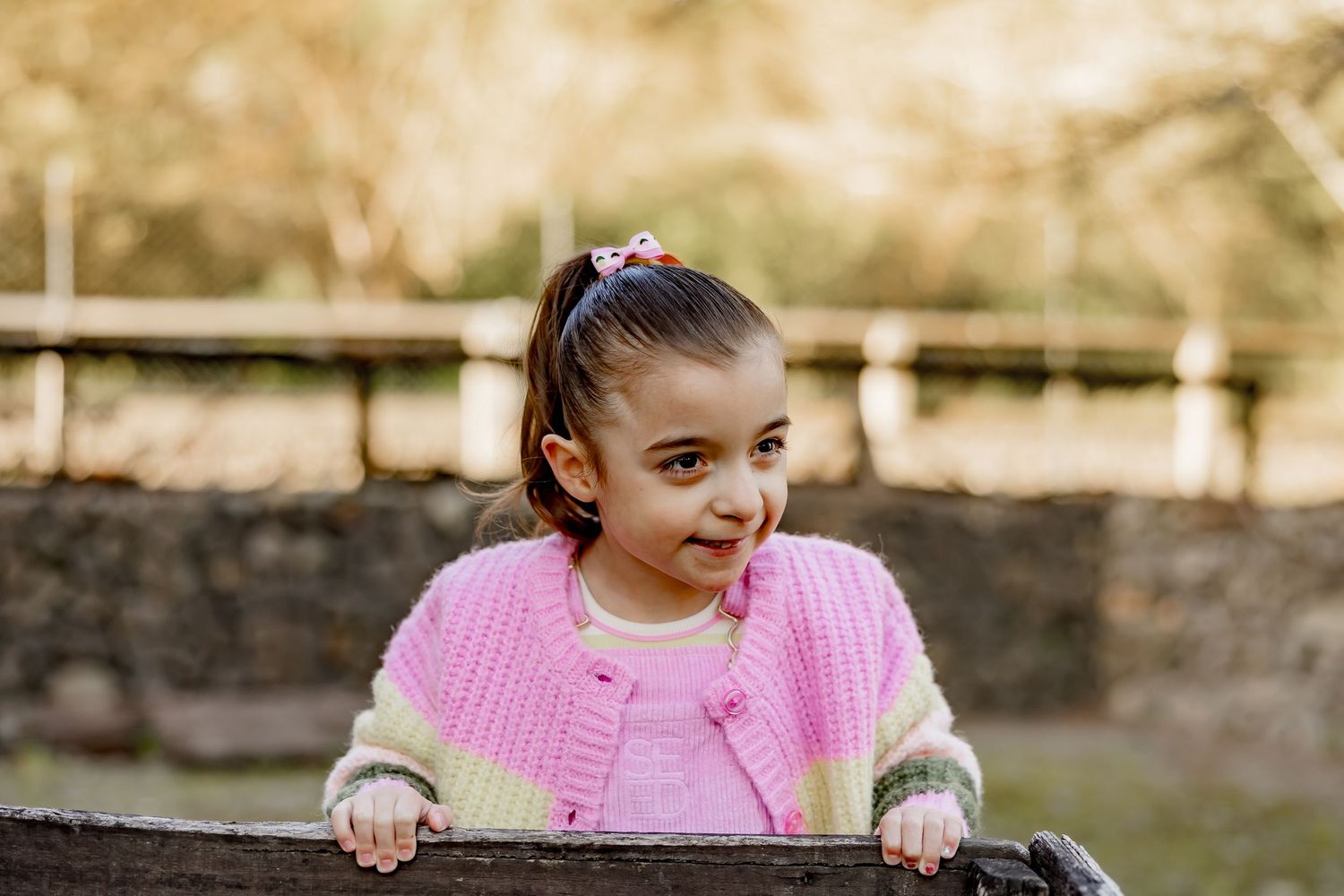 A person in a pink sweater laughs while riding a bicycle through a park on a sunny autumn day.