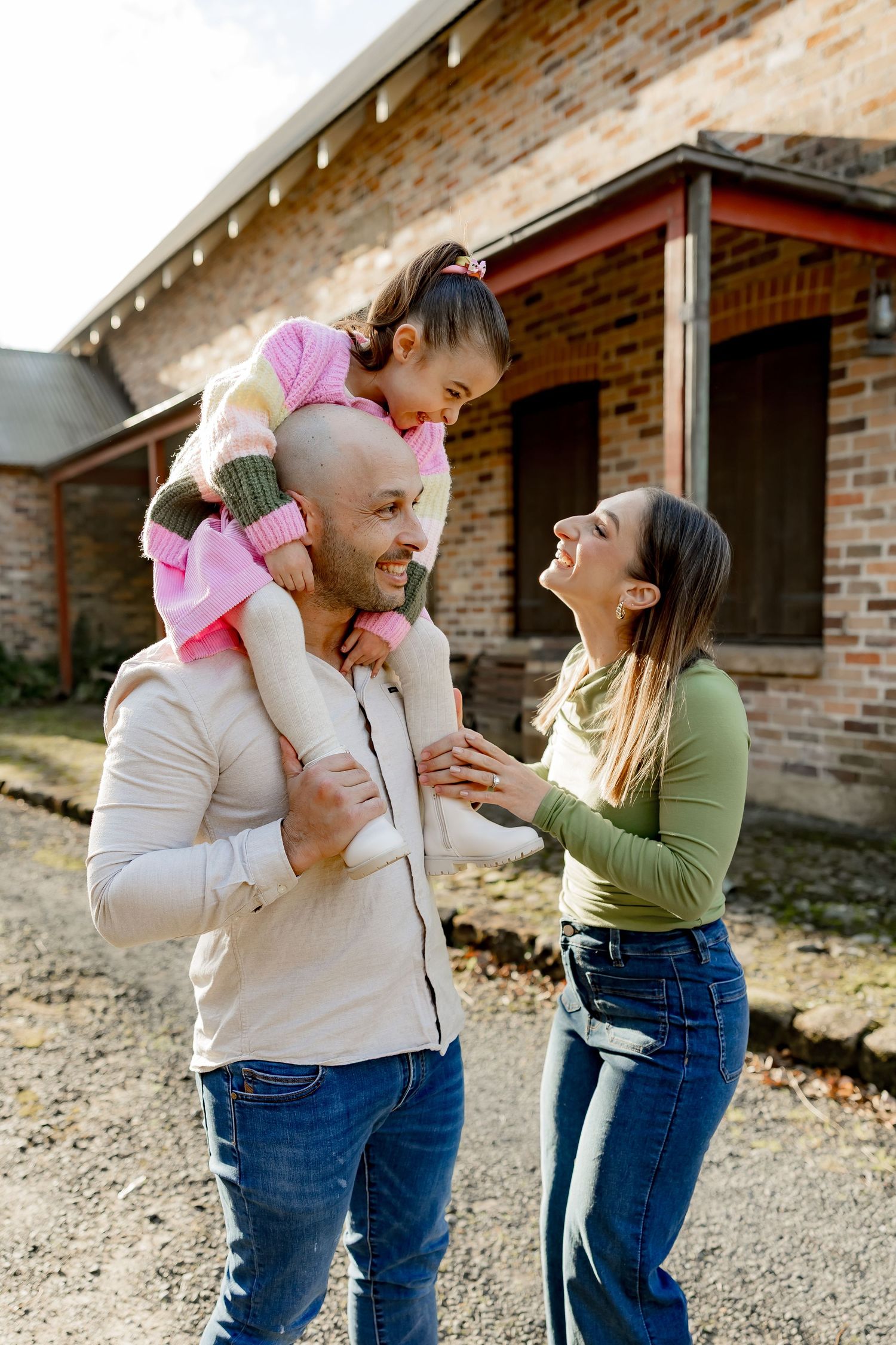 Family shares laughter and smiles during a playful outdoor moment by a brick building.