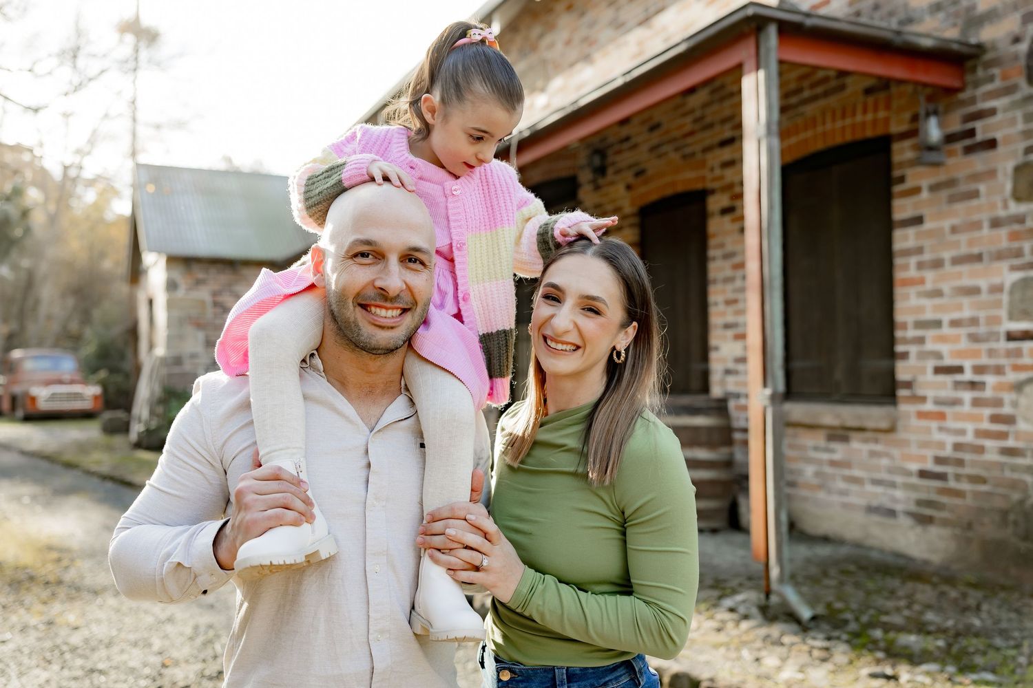 Family enjoying a sunny afternoon together outside their rustic brick home with cheerful smiles and warm lighting.