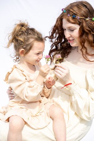A tender moment between mother and child in matching cream-colored dresses looking at something together.