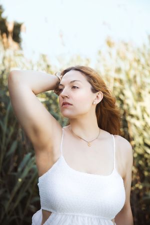 A person in a white sundress poses thoughtfully in front of tall grass during golden hour lighting.