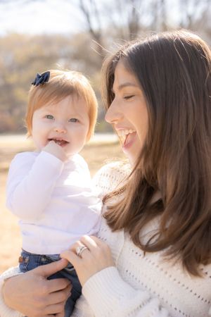 Joy filled moment shared between parent and baby outdoors on a sunny autumn day wearing matching white sweaters.