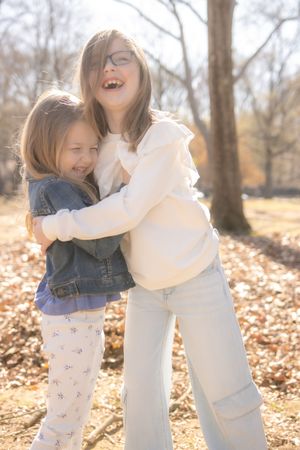 Two people share a joyful embrace and laugh together while standing in autumn leaves on a sunny day.