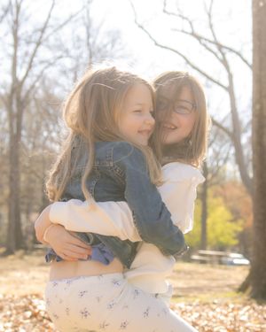 Two people share an intimate embrace and laugh joyfully together in a sunlit outdoor setting with autumn leaves.