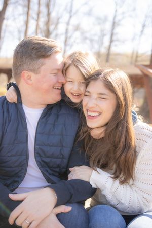 Family sharing joyful, candid moments together outdoors, wearing navy and cream colored clothing in a natural setting.