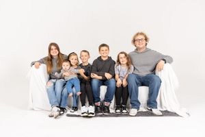 Family wearing blue jeans and white shirts sits casually together against a white background.